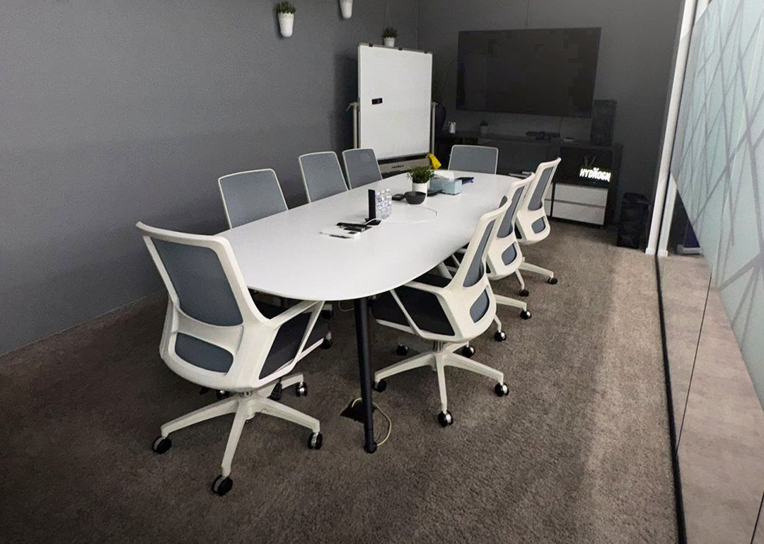 Meeting room with a white conference table, grey chairs and carpeted floor