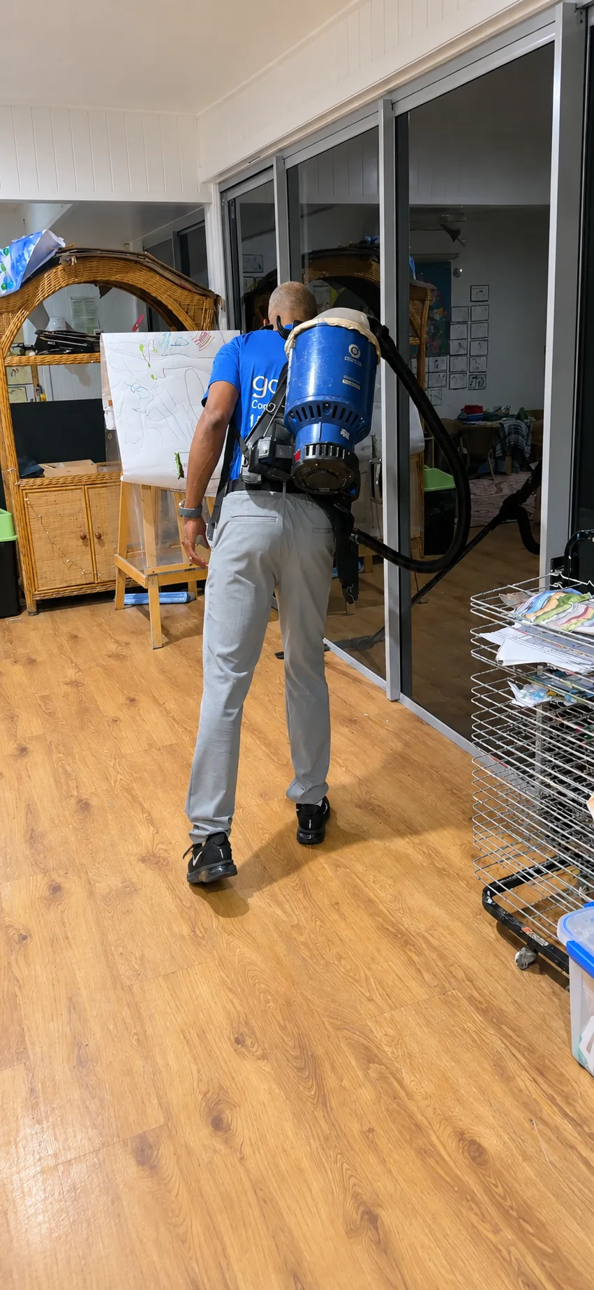 Gold Keys cleaner using a backpack vacuum on a hard floor beside glass doors